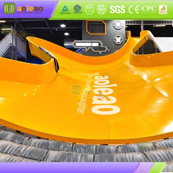 Giant yellow half-pipe slide equipment with a wide curved sliding surface in a commercial indoor amusement park